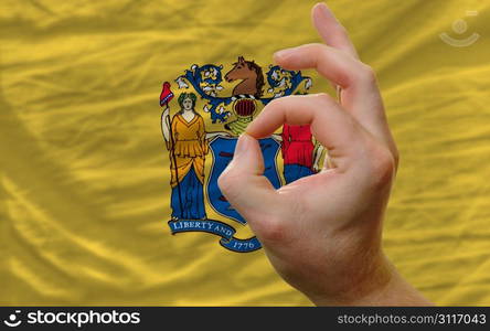 man showing excellence or ok gesture in front of complete wavy american state flag of new jersey symbolizing best quality, positivity and succes