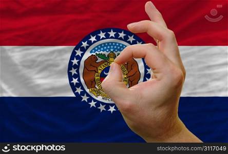 man showing excellence or ok gesture in front of complete wavy american state flag of missouri symbolizing best quality, positivity and succes