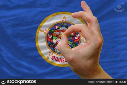 man showing excellence or ok gesture in front of complete wavy american state flag of minnesota symbolizing best quality, positivity and succes