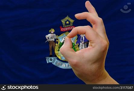 man showing excellence or ok gesture in front of complete wavy american state flag of maine symbolizing best quality, positivity and succes