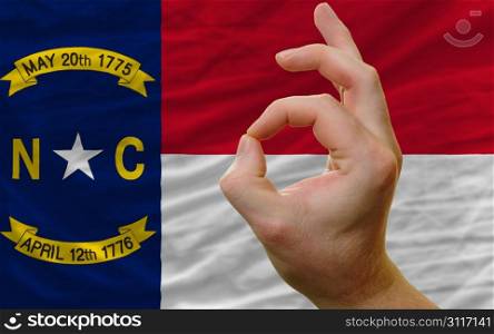 man showing excellence or ok gesture in front of complete wavy american state flag of north carolina symbolizing best quality, positivity and succes