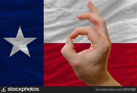 man showing excellence or ok gesture in front of complete wavy american state flag of texas symbolizing best quality, positivity and succes