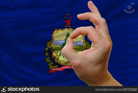 man showing excellence or ok gesture in front of complete wavy american state flag of vermont symbolizing best quality, positivity and succes