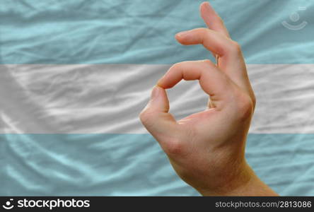 man showing excellence or ok gesture in front of complete wavy argentina national flag of symbolizing best quality, positivity and succes