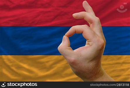 man showing excellence or ok gesture in front of complete wavy armenia national flag of symbolizing best quality, positivity and succes
