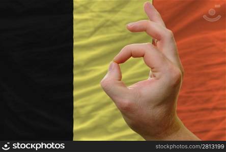 man showing excellence or ok gesture in front of complete wavy belgium national flag of symbolizing best quality, positivity and succes