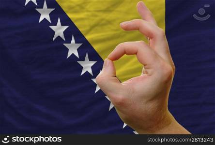 man showing excellence or ok gesture in front of complete wavy bosnia herzegovina national flag of symbolizing best quality, positivity and succes