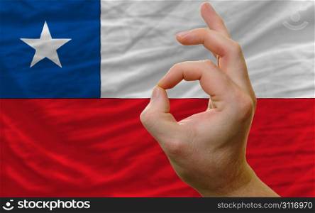 man showing excellence or ok gesture in front of complete wavy chile national flag of symbolizing best quality, positivity and succes