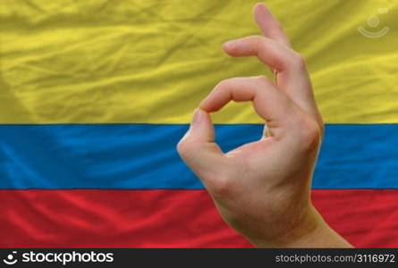 man showing excellence or ok gesture in front of complete wavy colombia national flag of symbolizing best quality, positivity and succes