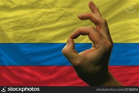 man showing excellence or ok gesture in front of complete wavy colombia national flag of symbolizing best quality, positivity and succes