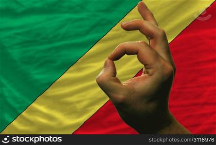 man showing excellence or ok gesture in front of complete wavy congo national flag of symbolizing best quality, positivity and succes