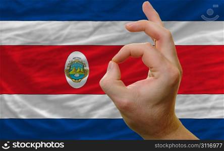 man showing excellence or ok gesture in front of complete wavy costa rica national flag of symbolizing best quality, positivity and succes