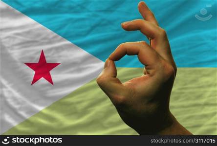 man showing excellence or ok gesture in front of complete wavy djibouti national flag of symbolizing best quality, positivity and succes