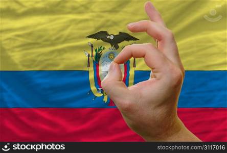 man showing excellence or ok gesture in front of complete wavy ecuador national flag of symbolizing best quality, positivity and succes