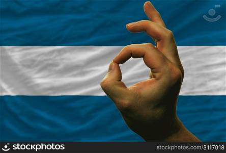 man showing excellence or ok gesture in front of complete wavy el salvador national flag of symbolizing best quality, positivity and succes