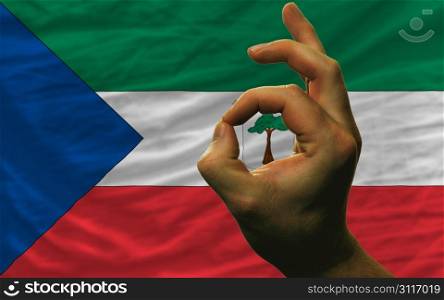 man showing excellence or ok gesture in front of complete wavy equatorial guinea national flag of symbolizing best quality, positivity and succes