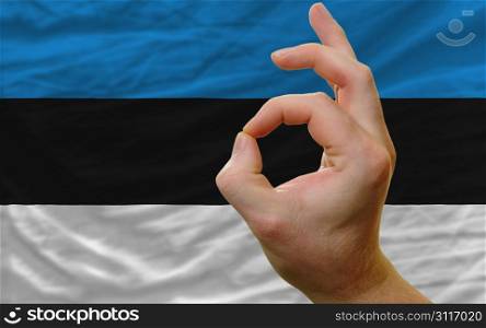 man showing excellence or ok gesture in front of complete wavy estonia national flag of symbolizing best quality, positivity and succes