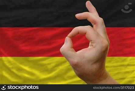 man showing excellence or ok gesture in front of complete wavy germany national flag of symbolizing best quality, positivity and succes