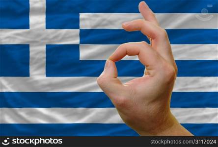 man showing excellence or ok gesture in front of complete wavy greece national flag of symbolizing best quality, positivity and succes