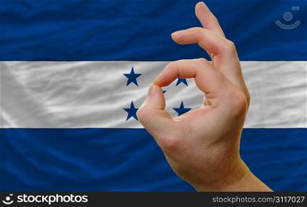 man showing excellence or ok gesture in front of complete wavy honduras national flag of symbolizing best quality, positivity and succes