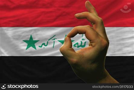 man showing excellence or ok gesture in front of complete wavy iraq national flag of symbolizing best quality, positivity and succes