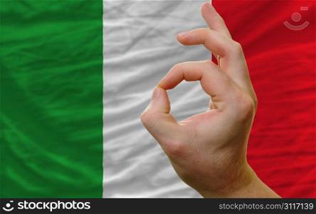 man showing excellence or ok gesture in front of complete wavy italy national flag of symbolizing best quality, positivity and succes