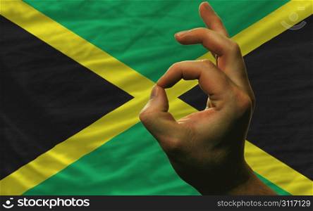 man showing excellence or ok gesture in front of complete wavy jamaica national flag of symbolizing best quality, positivity and succes