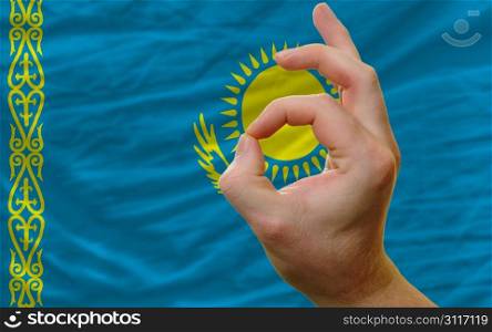 man showing excellence or ok gesture in front of complete wavy kazakhstan national flag of symbolizing best quality, positivity and succes