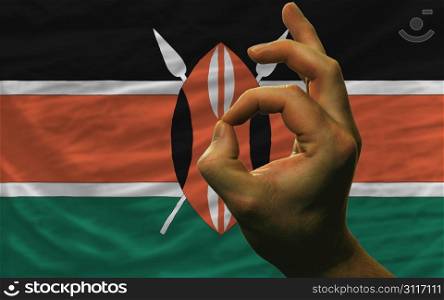 man showing excellence or ok gesture in front of complete wavy kenya national flag of symbolizing best quality, positivity and succes