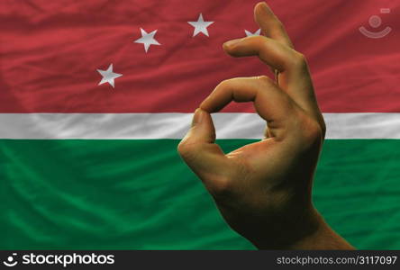 man showing excellence or ok gesture in front of complete wavy maghreb national flag of symbolizing best quality, positivity and succes