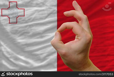 man showing excellence or ok gesture in front of complete wavy malta national flag of symbolizing best quality, positivity and succes