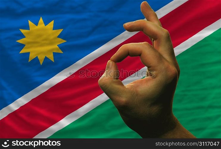 man showing excellence or ok gesture in front of complete wavy namibia national flag of symbolizing best quality, positivity and succes