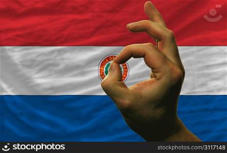 man showing excellence or ok gesture in front of complete wavy paraguay national flag of symbolizing best quality, positivity and succes