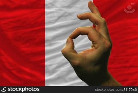 man showing excellence or ok gesture in front of complete wavy peru national flag symbolizing best quality, positivity and succes