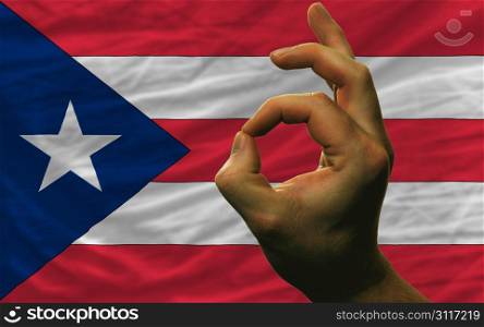 man showing excellence or ok gesture in front of complete wavy puerto rico national flag symbolizing best quality, positivity and succes