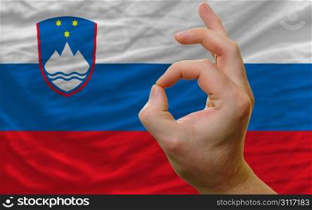 man showing excellence or ok gesture in front of complete wavy slovenia national flag symbolizing best quality, positivity and succes