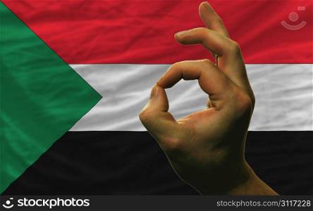 man showing excellence or ok gesture in front of complete wavy sudan national flag symbolizing best quality, positivity and succes