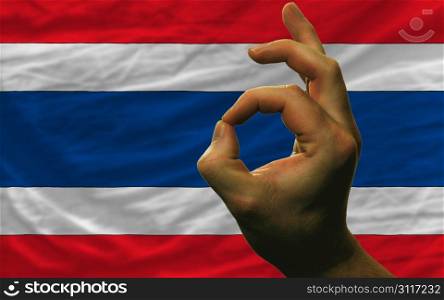 man showing excellence or ok gesture in front of complete wavy thailand national flag of symbolizing best quality, positivity and succes