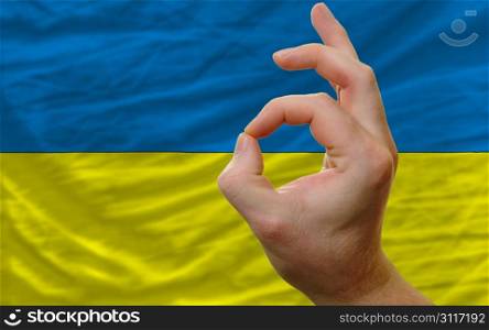man showing excellence or ok gesture in front of complete wavy ukraine national flag of symbolizing best quality, positivity and succes