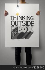 man showing poster of hand drawn word THINKING OUTSIDE OF THE BOX with growing lightbulb as concept
