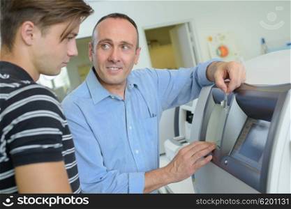 Man showing younger man how to use cash machine