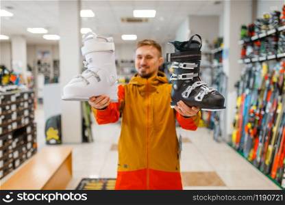 Man shows white and black ski or snowboarding boots in sports shop. Winter season extreme lifestyle, active leisure, male customer with protect equipment