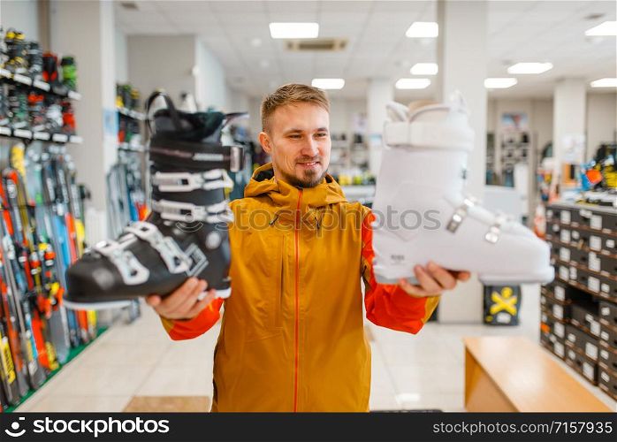 Man shows white and black ski or snowboarding boots in sports shop. Winter season extreme lifestyle, active leisure, male customer with protect equipment. Man shows ski or snowboarding boots in sports shop
