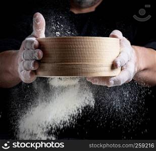 man sifts white wheat flour through a wooden sieve, close up