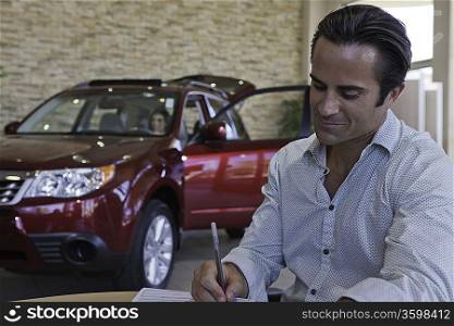 Man signing papers with car in background