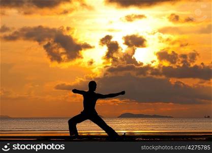 Man silhouette doing yoga exercise archer at sunset beach