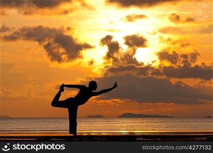 Man silhouette doing yoga exercise natarja at sunset beach
