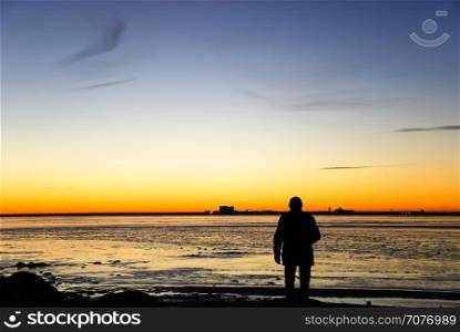 Man silhouette watching the skyline of the swedish city Kalmar in the horizon by sunset