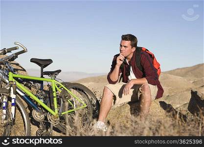 Man sits on rock thinking with mountain bikes