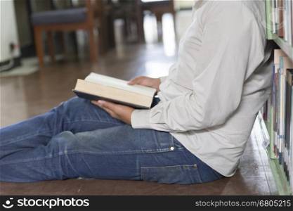 man sitting and reading book on floor in aisle in library